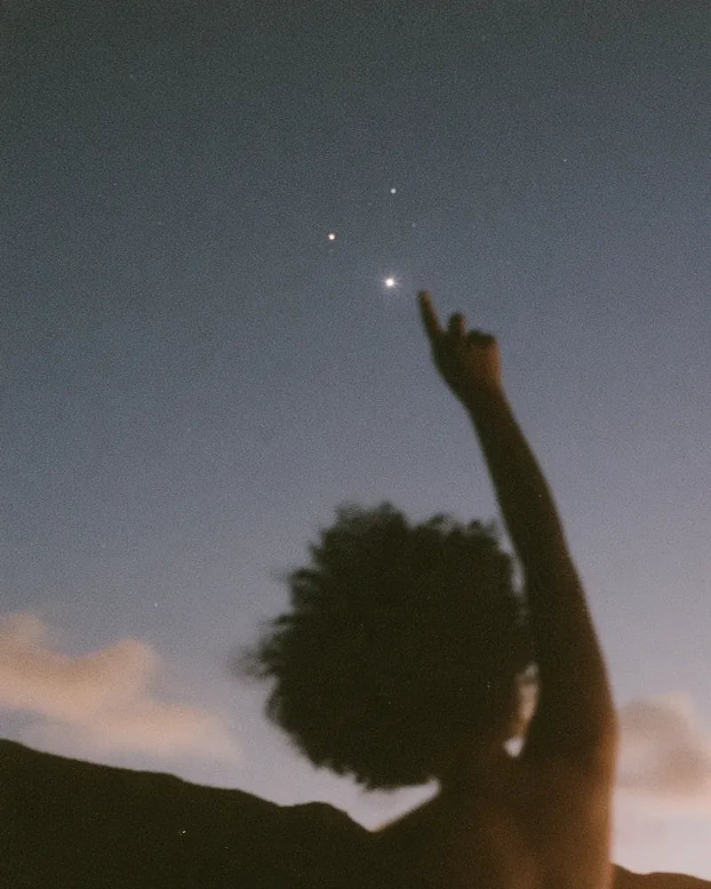 Someone pointing up at the first stars in a dusk sky.